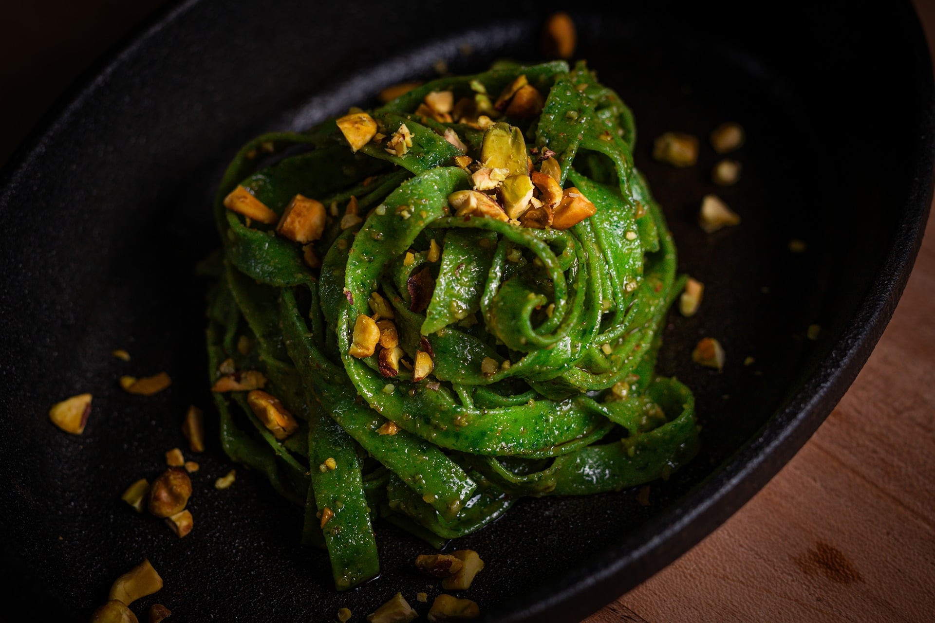 Pasta verde con pistachos servida en un plato oscuro
